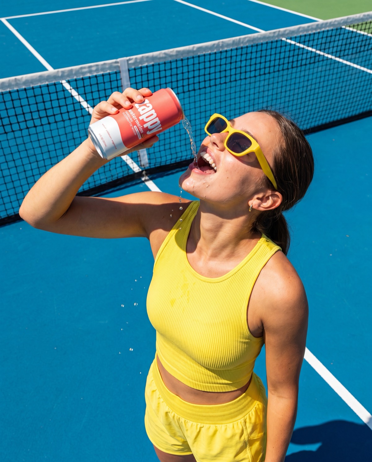Tennis player in yellow drinking a cold can of Zappy on a blue court